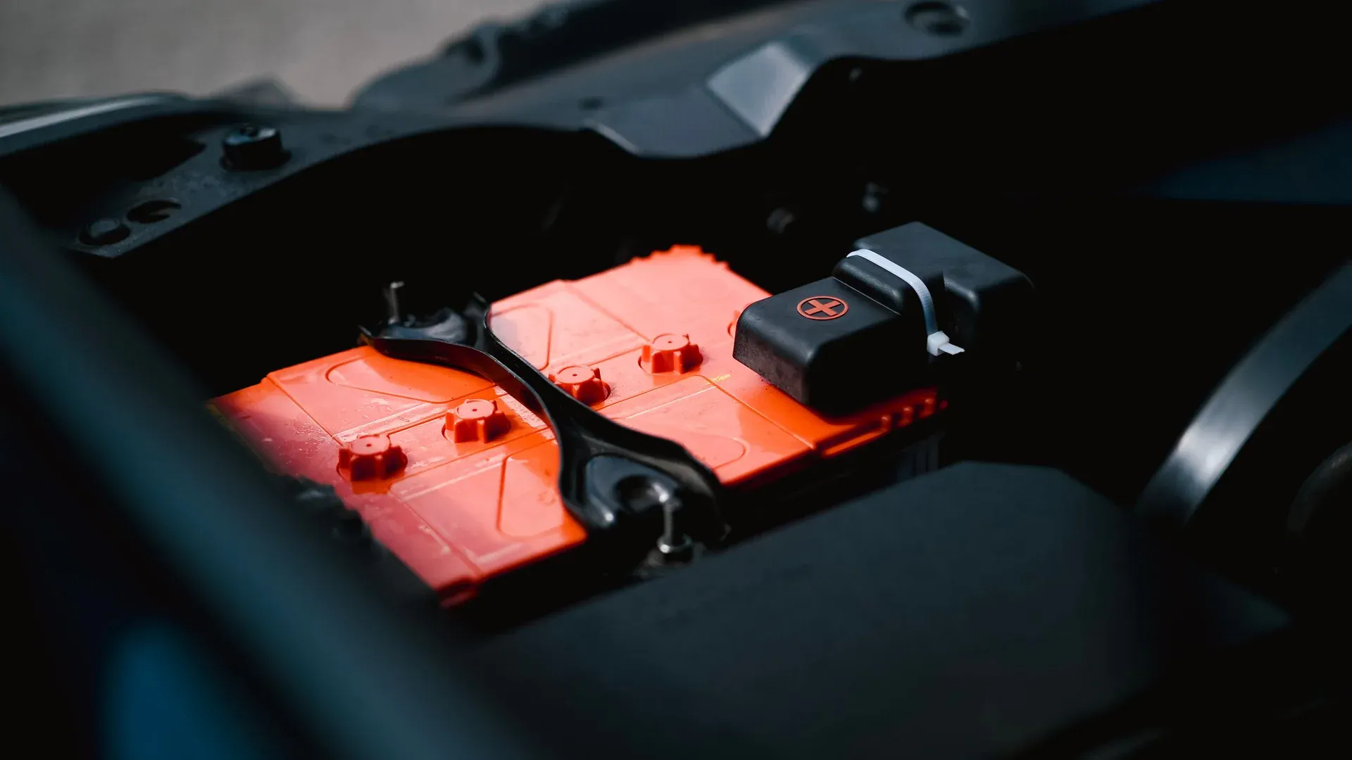 Detailed view of an orange car battery inside a vehicle's engine bay, highlighting its features