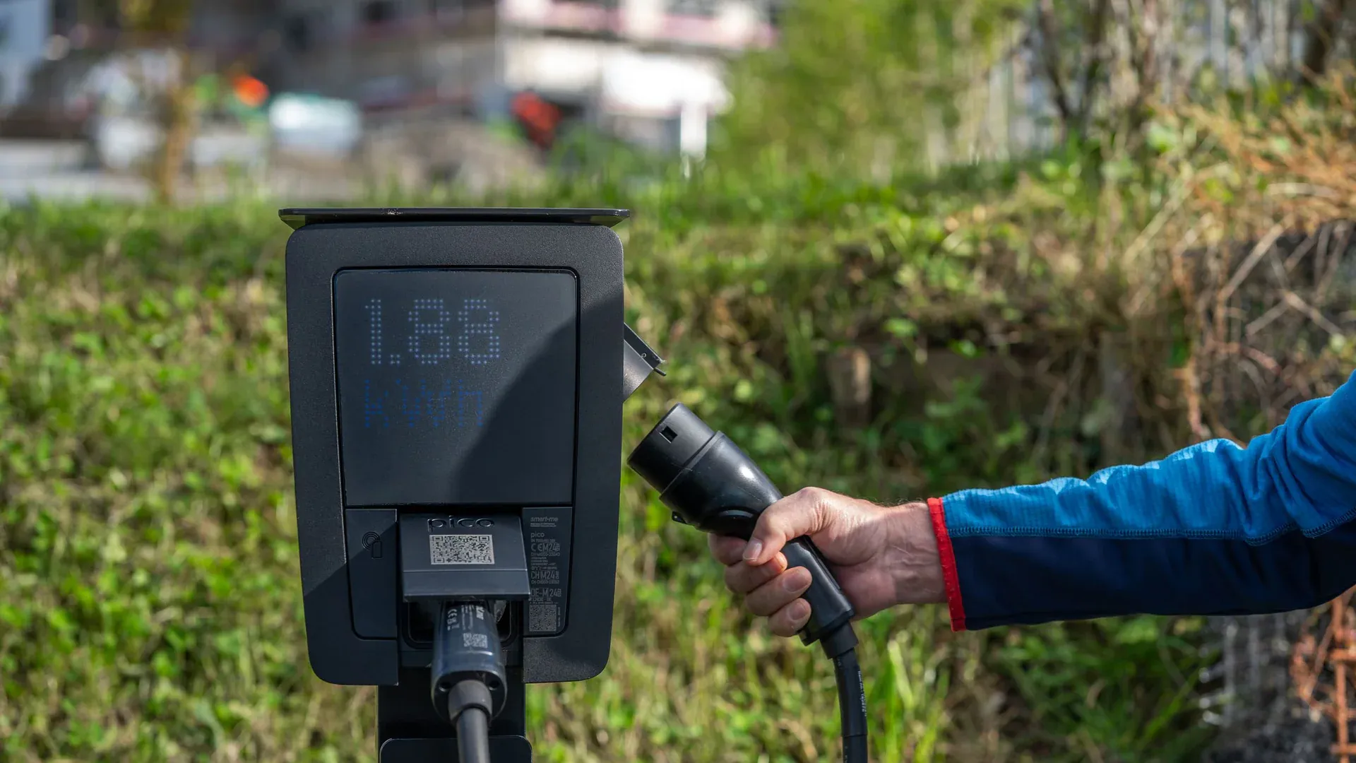 An outdoor electric car charging station with a hand holding a charging cable