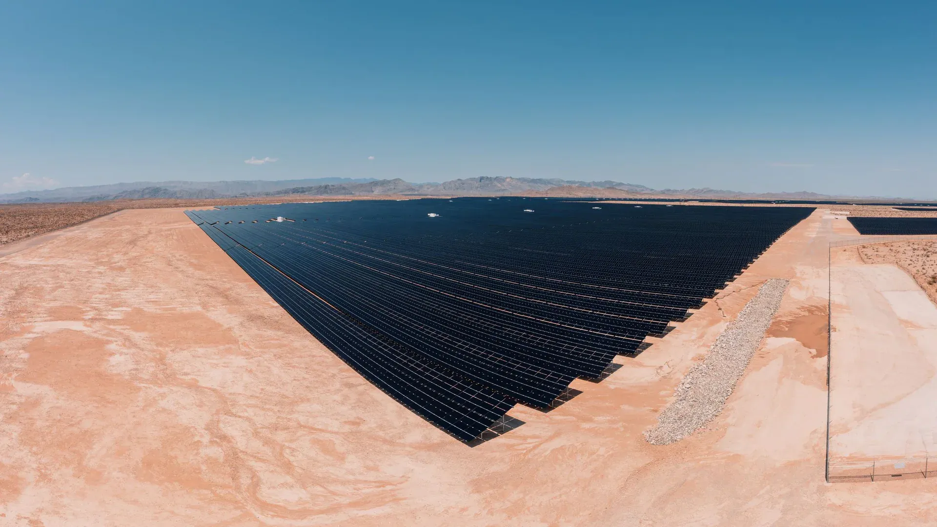 Aerial view of a large solar farm in a desert setting under a clear blue sky