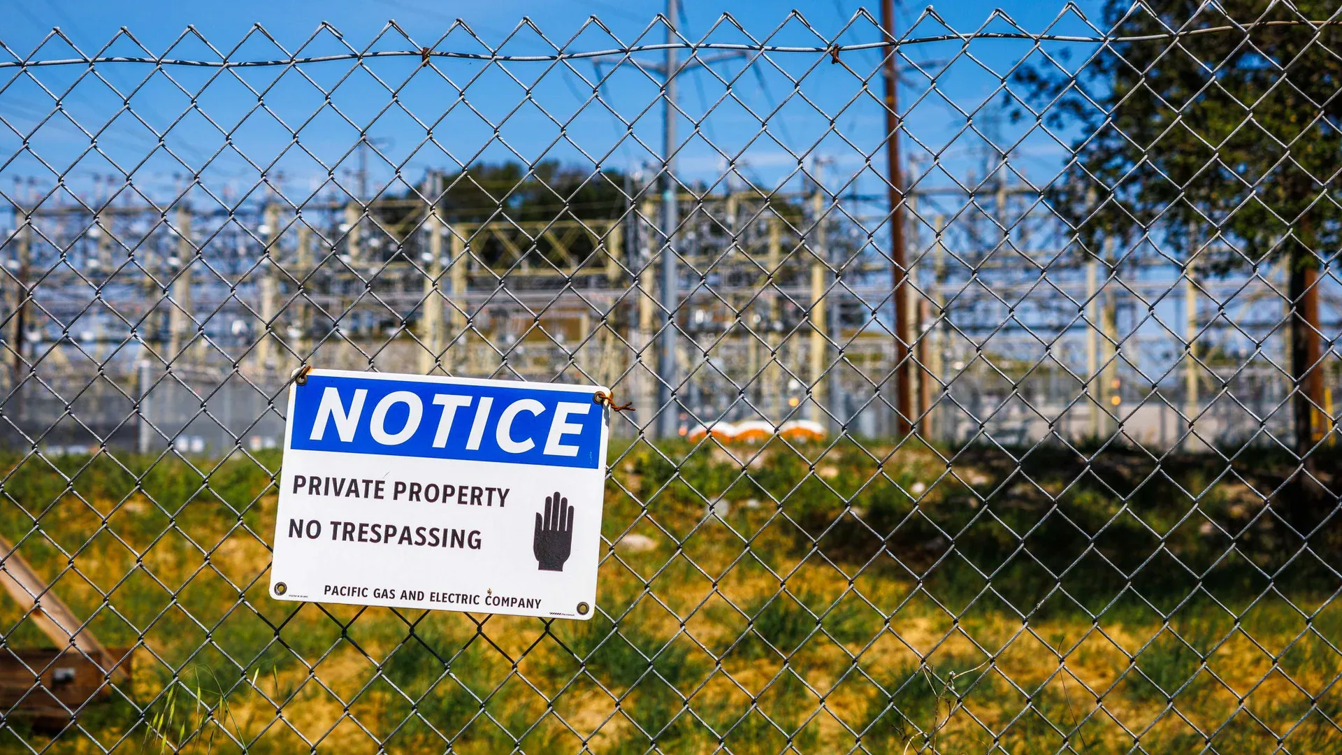 Chain link fence with a private property no trespassing notice sign and electrical infrastructure in the background