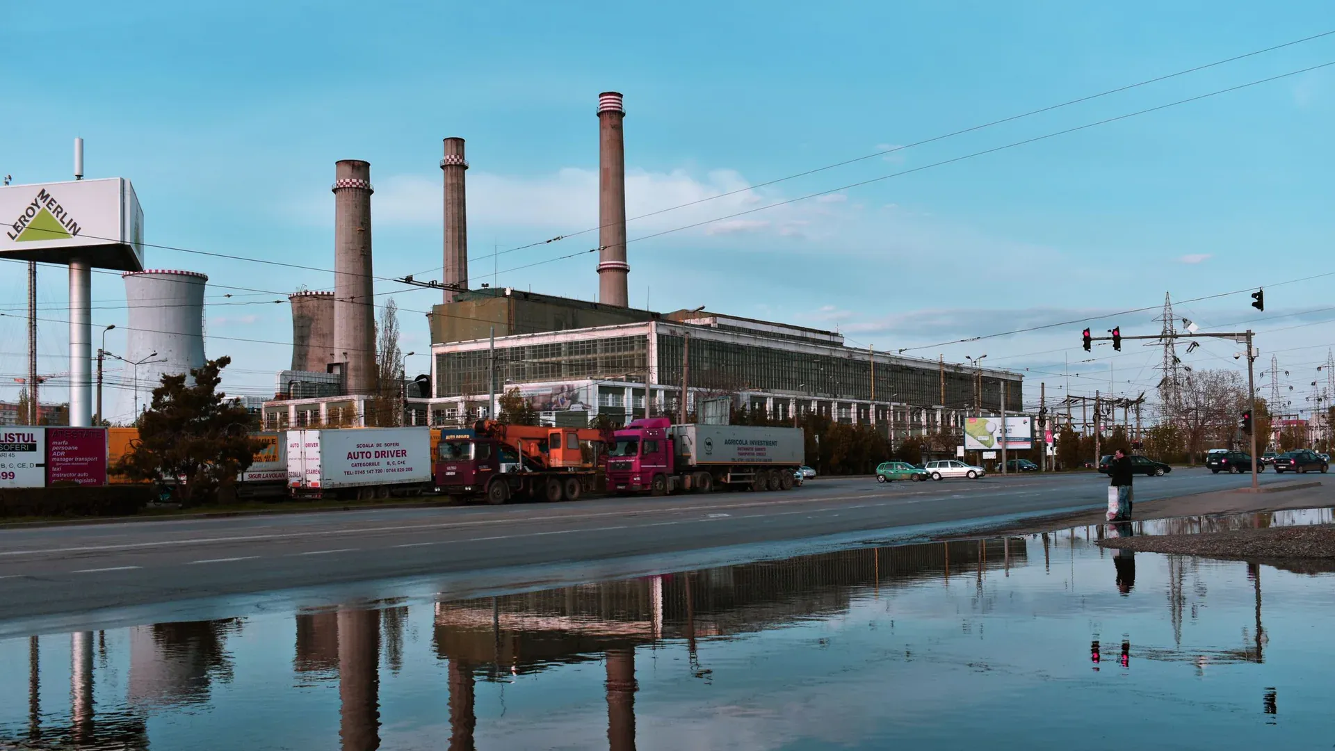 Industrial plant with road and trucks in Iași, Romania, reflecting in water on a sunny day