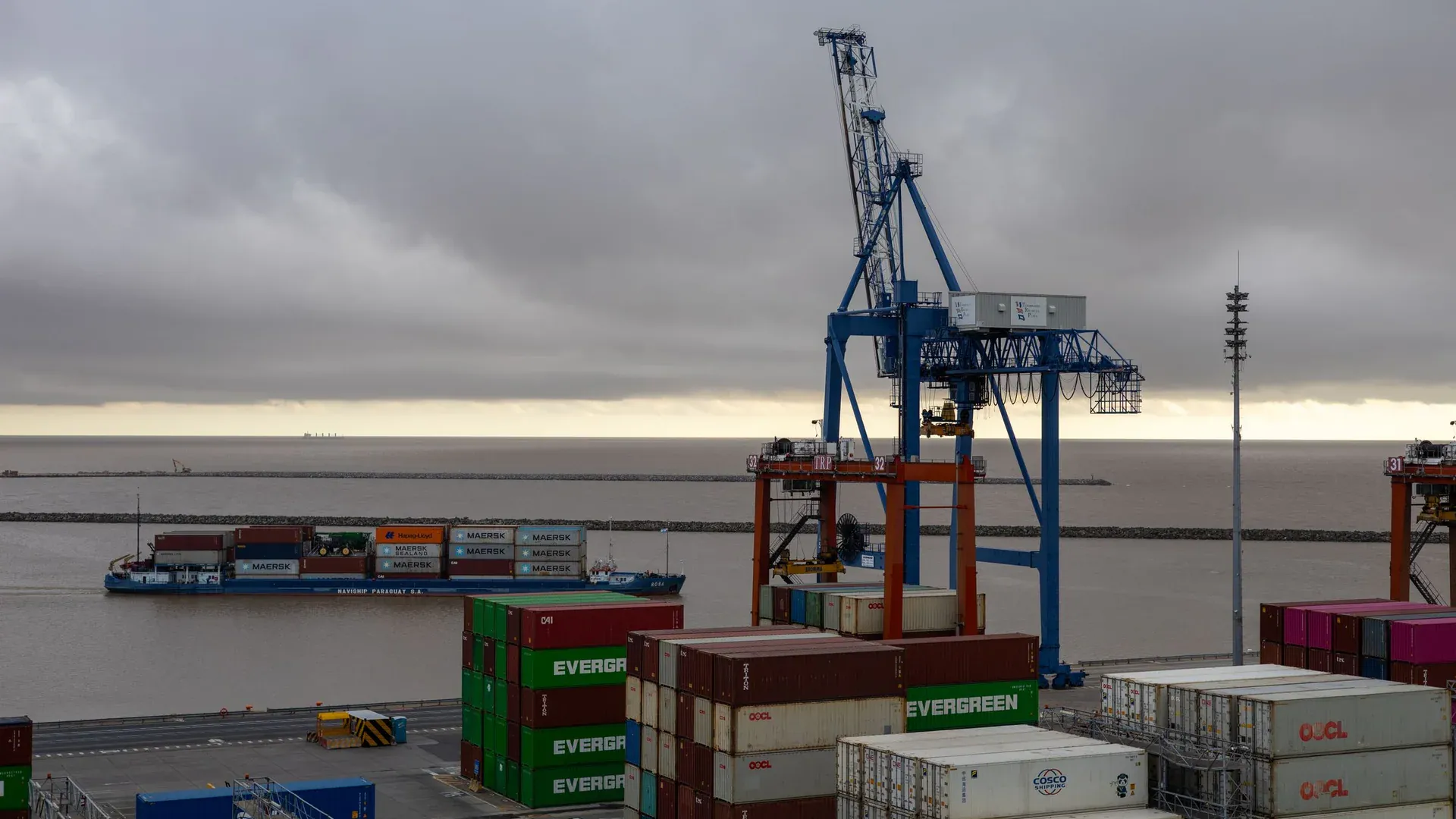 Large cargo cranes at a shipping port with stacked containers and cargo ship