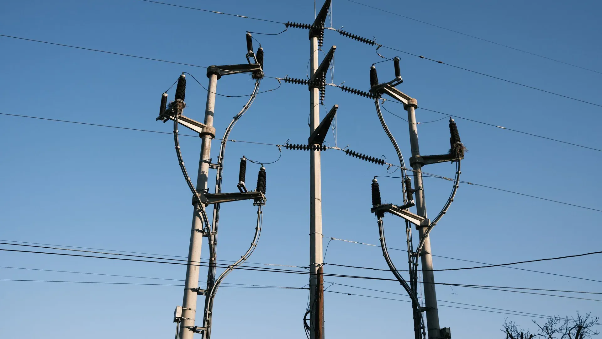 High-voltage power lines and poles silhouetted against a clear blue sky, representing energy distribution