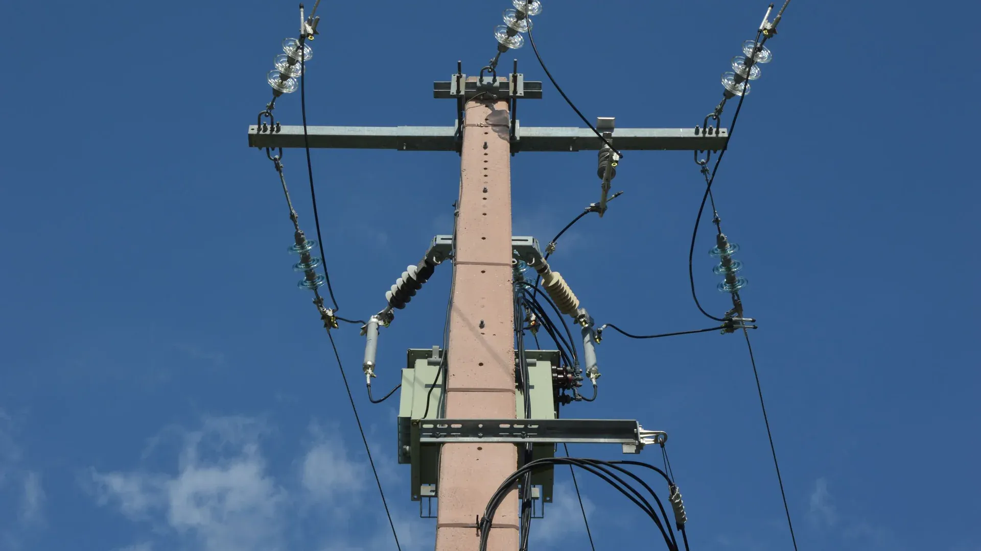 Low angle view of a utility pole with power lines against a blue sky
