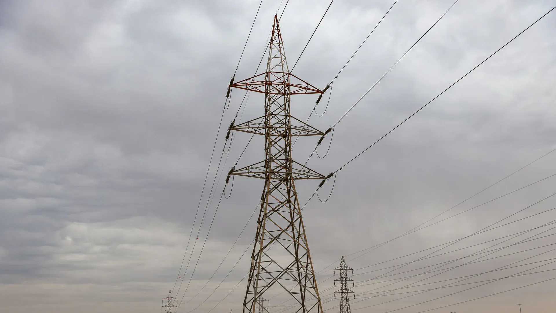 Power transmission towers under a cloudy sky spanning across a desert landscape, showcasing industrial infrastructure