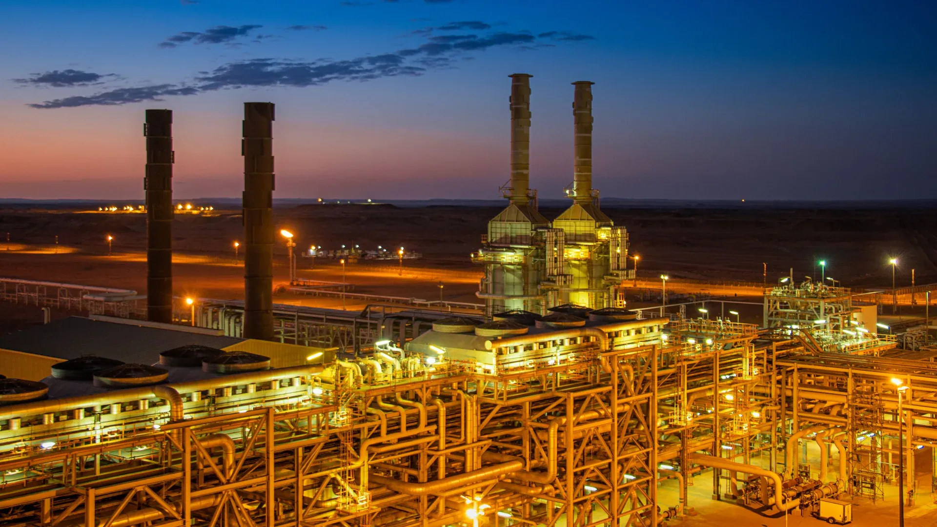 Aerial view of an illuminated factory with chimneys at sunset, showcasing industrial architecture