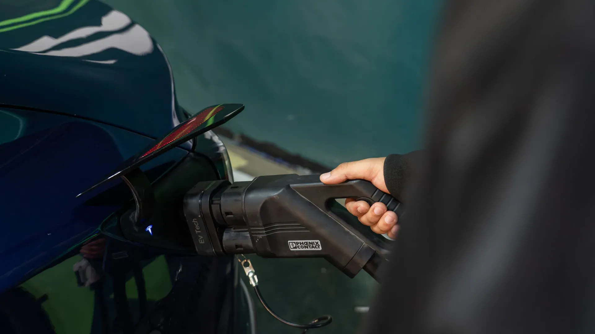 Driver holding an EV charging connector beside an electric car