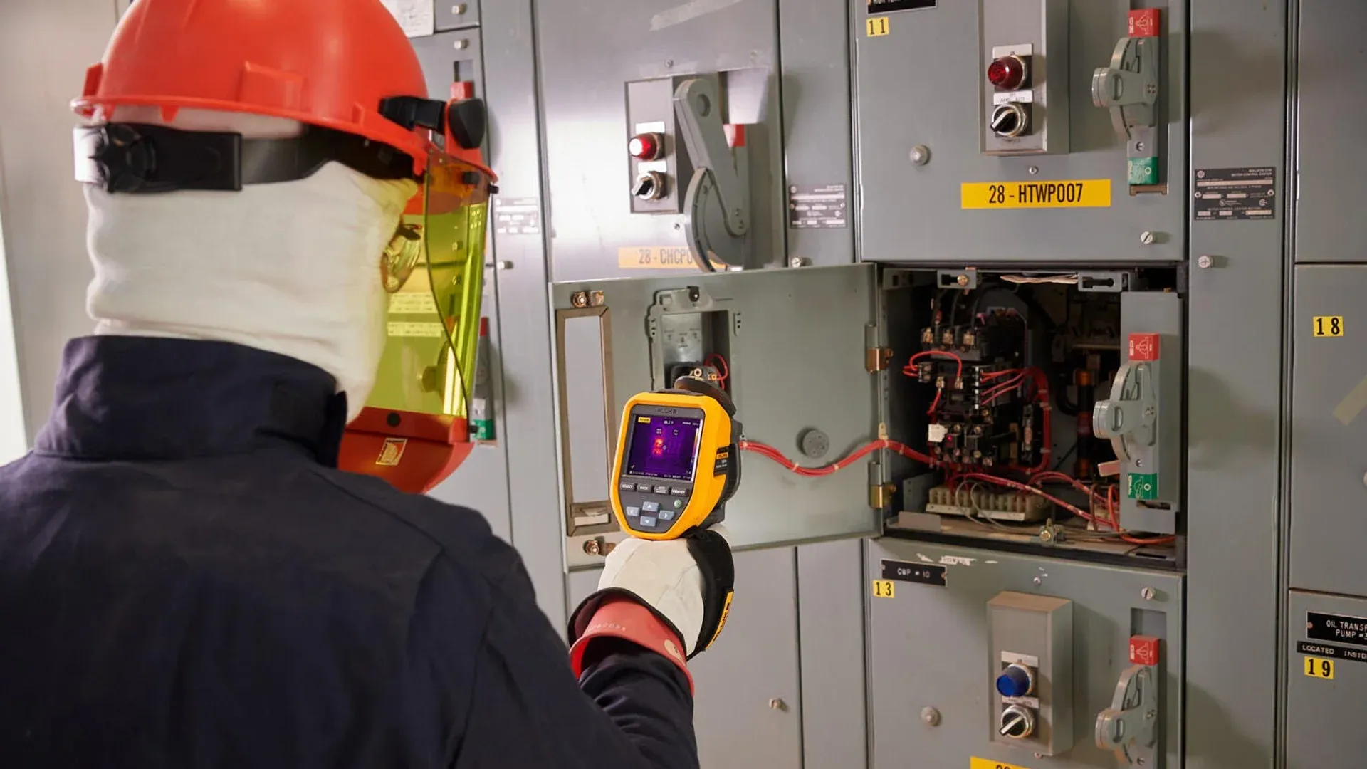 Electrical inspector aiming a handheld thermal imager at open switchgear
