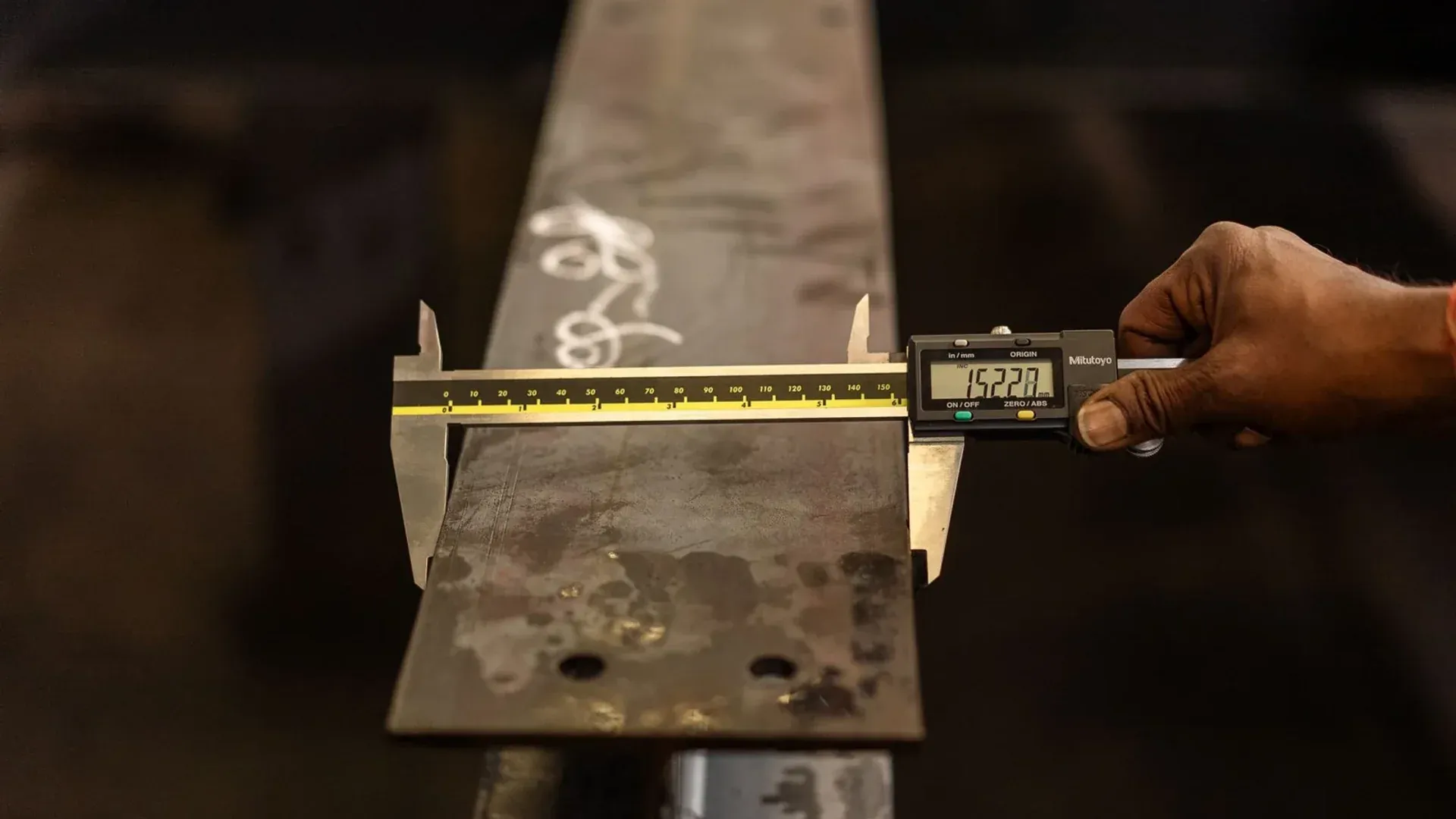 An inspector measuring a metal bar with a digital caliper