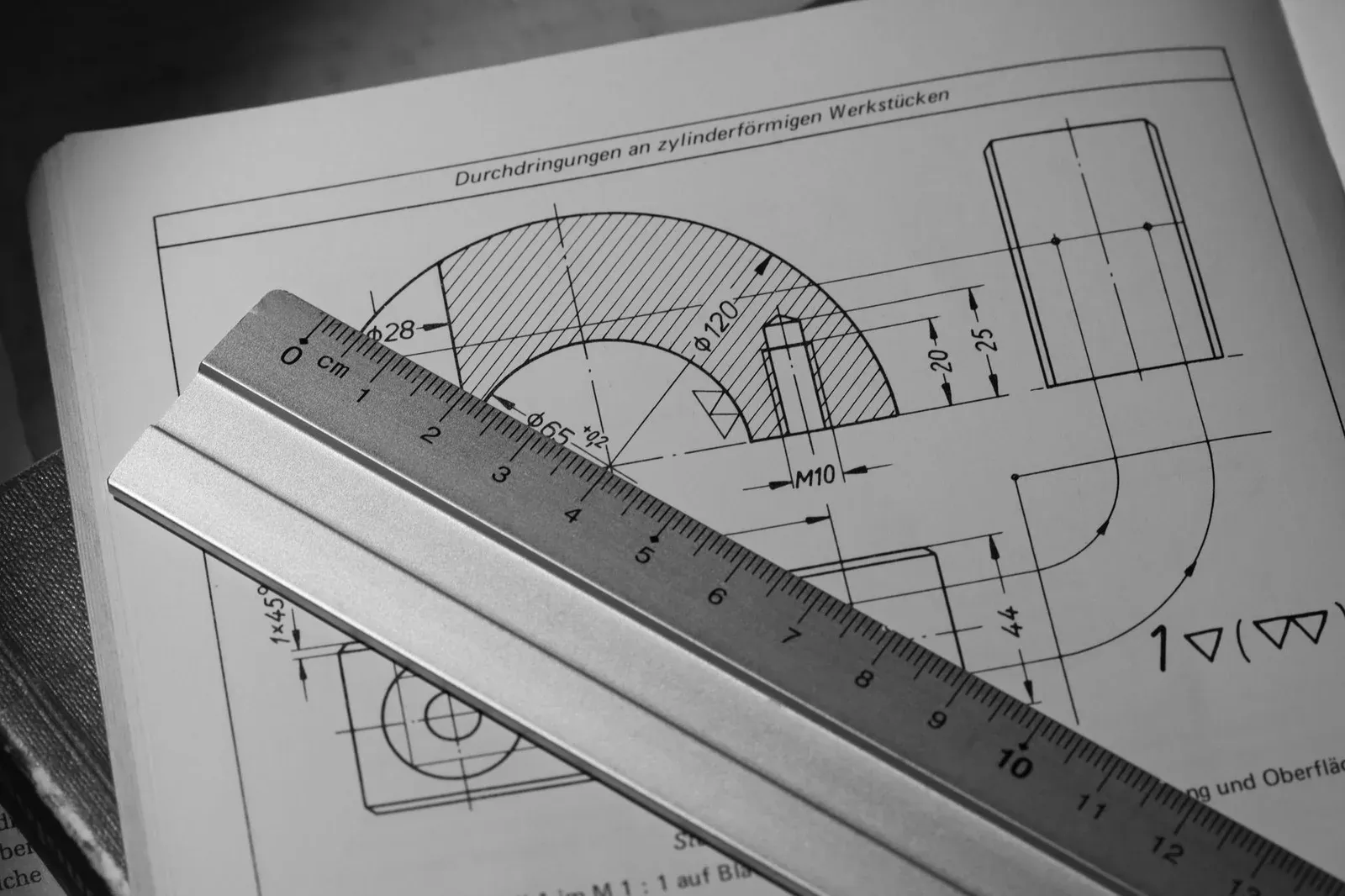 Metal ruler placed over a dimensioned technical drawing