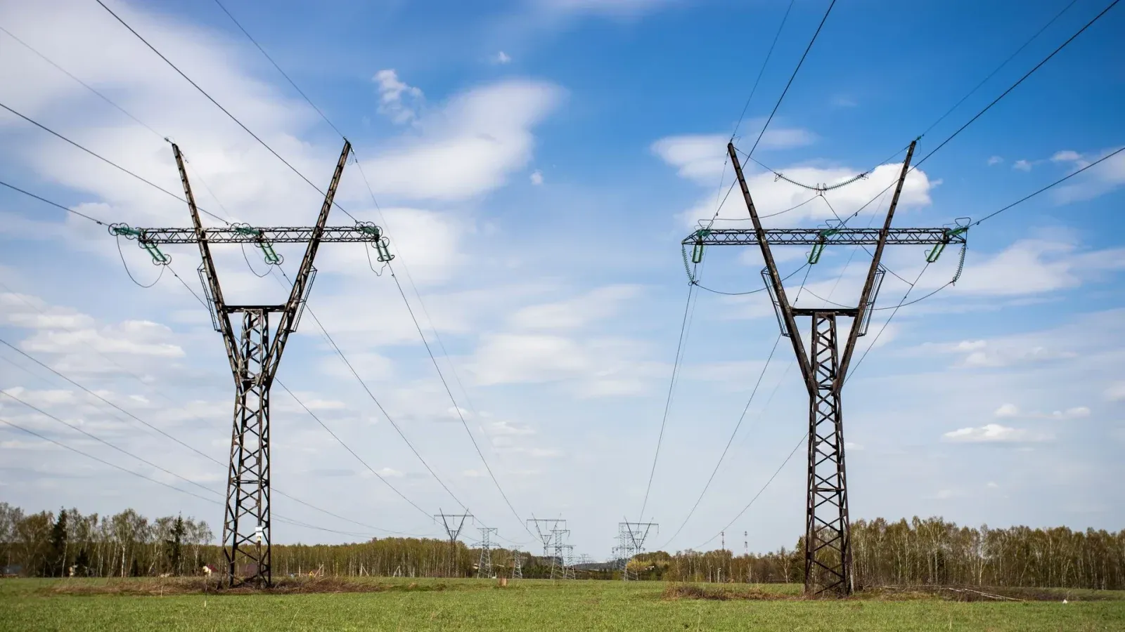 High-voltage transmission towers and overhead power lines crossing open terrain representing grid infrastructure