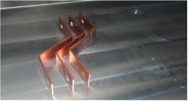 Two formed copper busbar samples with offset bends and mounting holes on a metal worktable