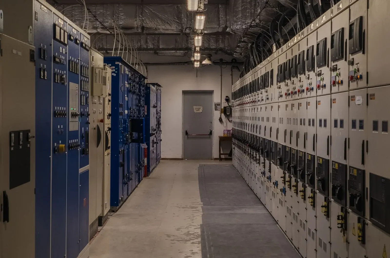 Two rows of industrial switchgear cabinets facing a central aisle