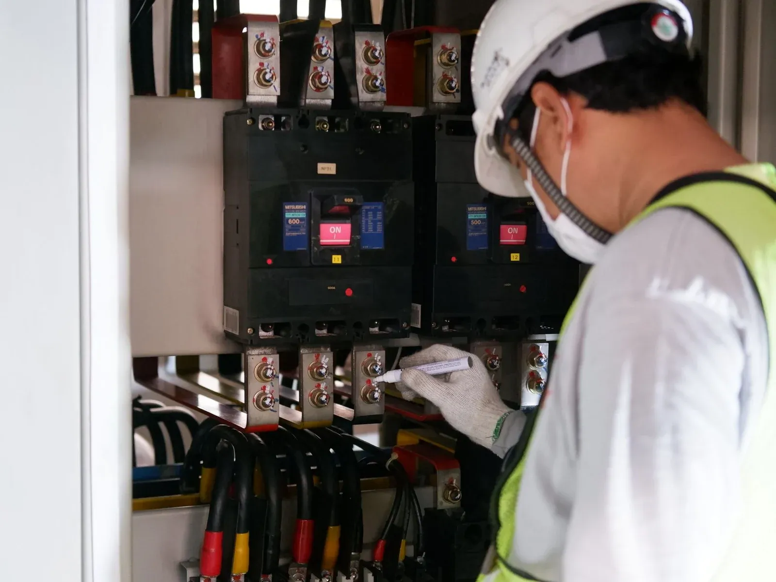 Technician wearing protective equipment inspecting conductors inside an electrical panel