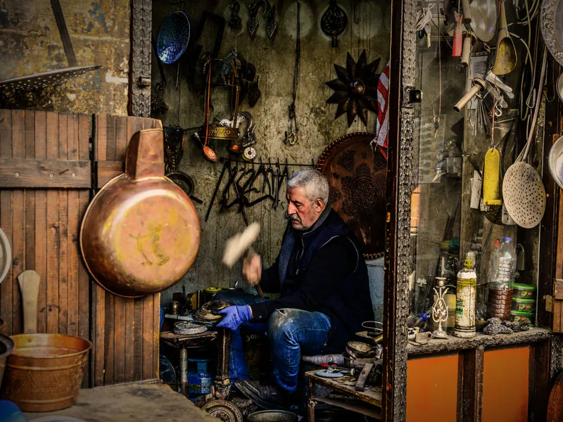 An artisan crafting metal items in a vintage workshop, surrounded by tools and decor