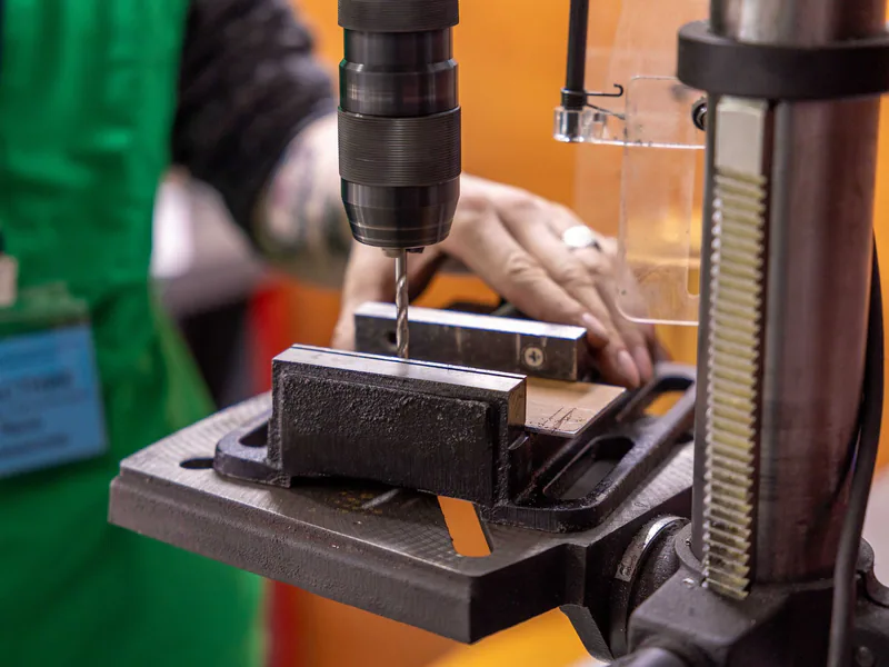 Detailed view of a hand operating a drill press in a workshop setting