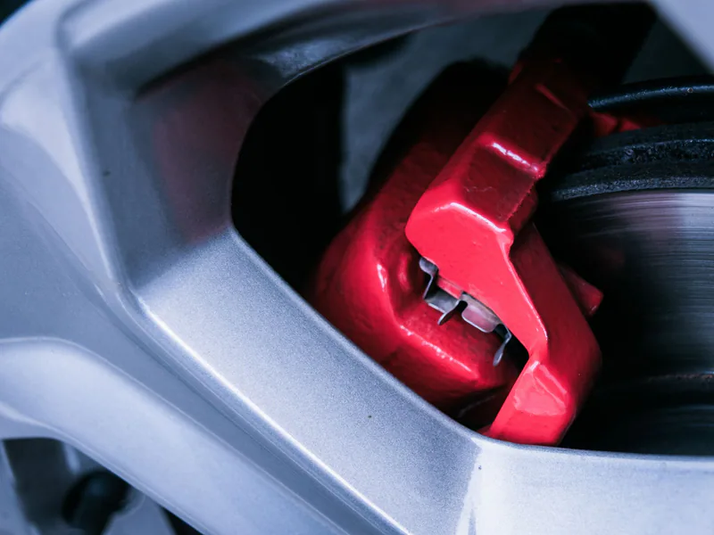 Detailed photo of a red automotive brake caliper and disc brake in focus
