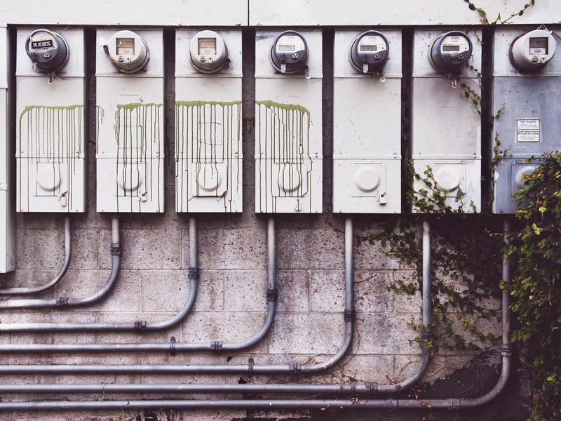 Array of outdoor electric meters on a brick wall with vines