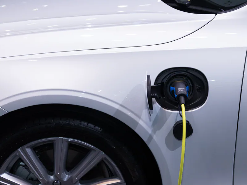 A white electric car is plugged in for charging, close-up view of the charging port