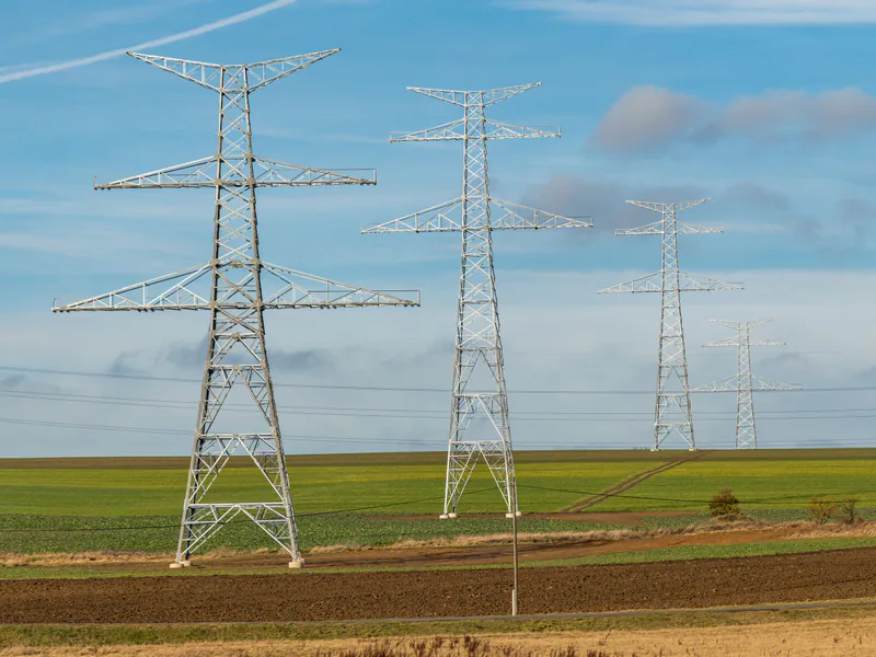 Series of transmission towers on green fields under blue skies, symbolizing energy distribution
