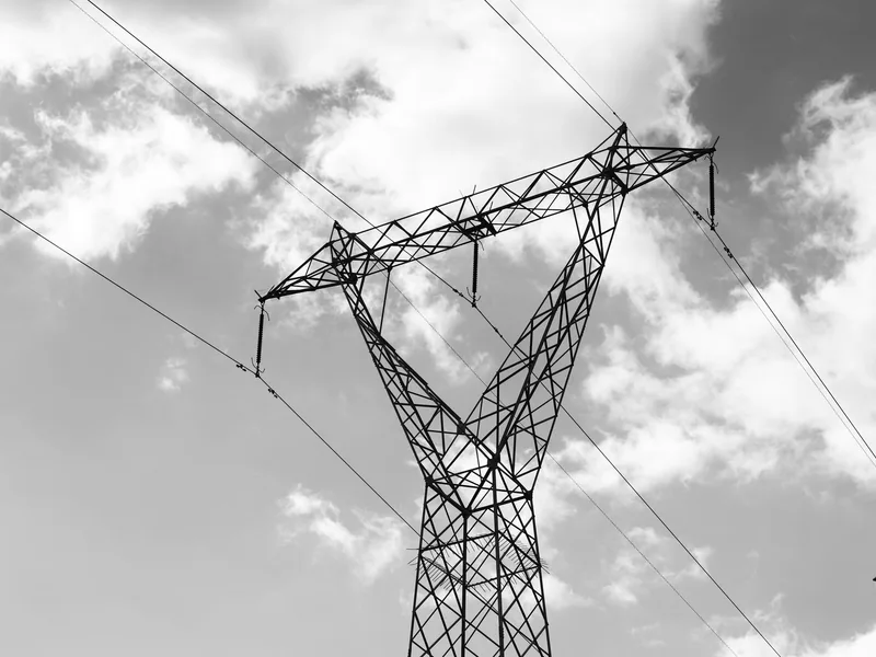 A high voltage power line towering against a dramatic cloudy sky in a black and white composition