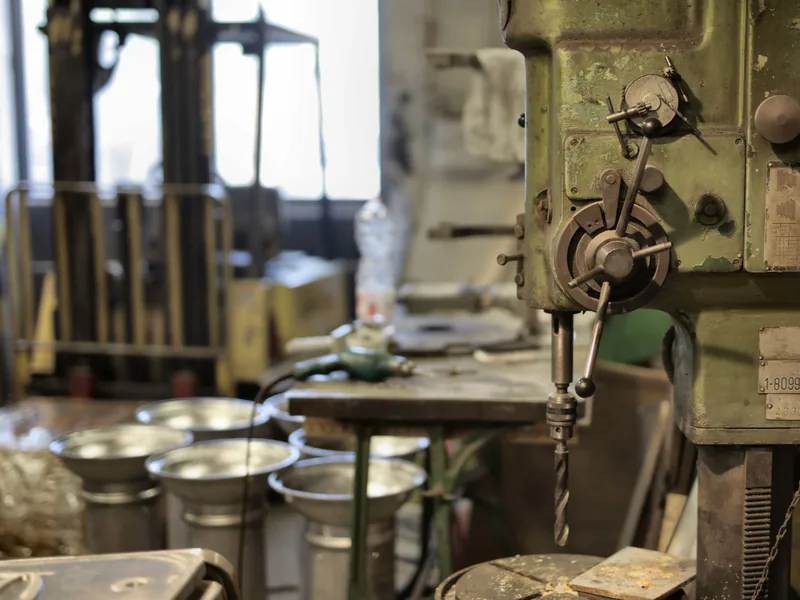Side view of industrial drilling machine with green casing situated in deserted workshop