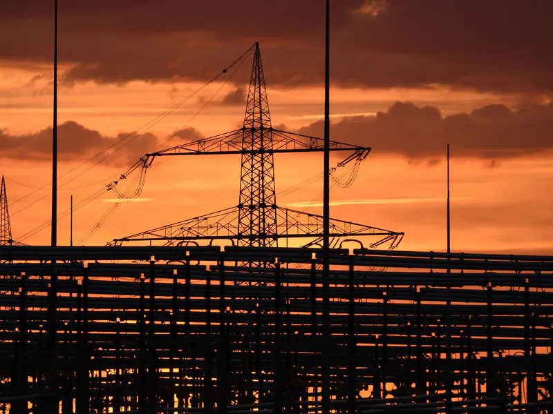 Silhouetted electric tower against vivid sunset sky, highlighting urban infrastructure