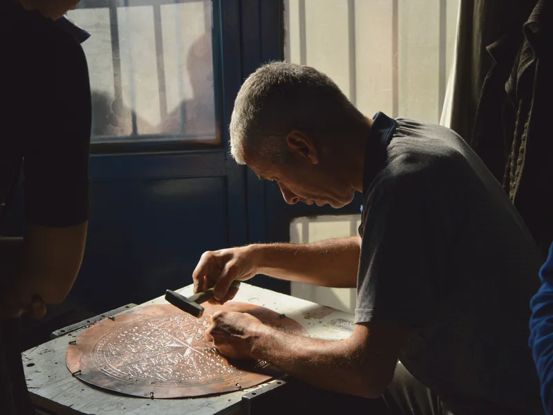 Skilled artisan meticulously hammering a design onto a copper plate in natural light