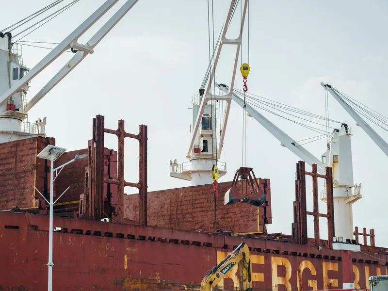 Cargo ship docked at an industrial port with cranes unloading cargo under clear skies