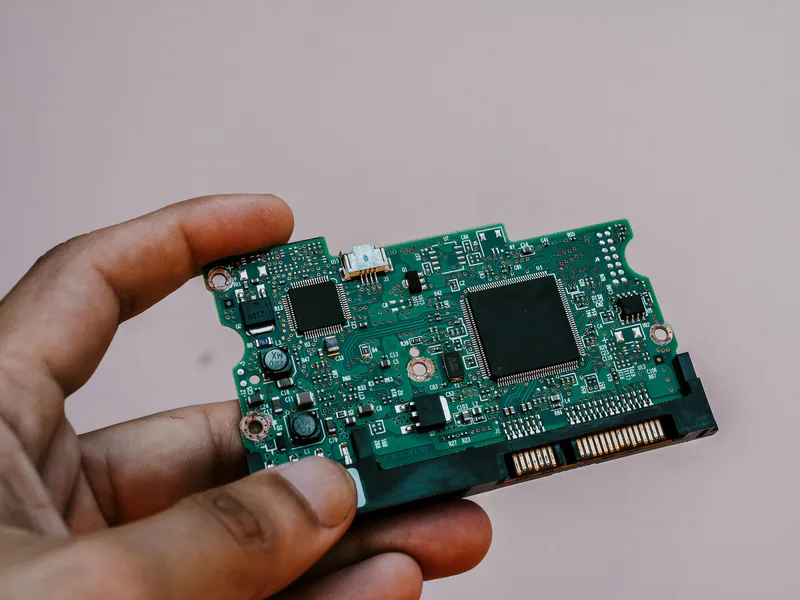 Close-up image of a hand holding a circuit board from a hard drive, showcasing electronic technology