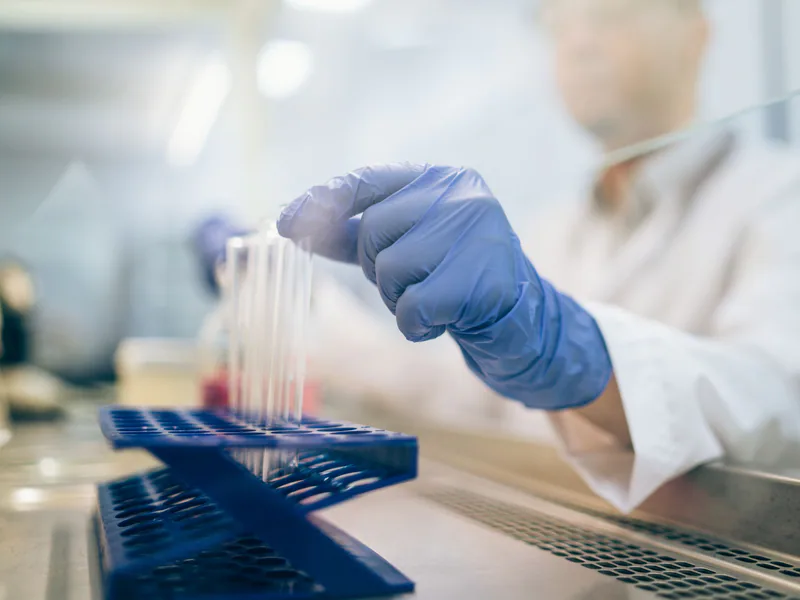Close-up of a scientist wearing gloves and handling test tubes in a laboratory environment