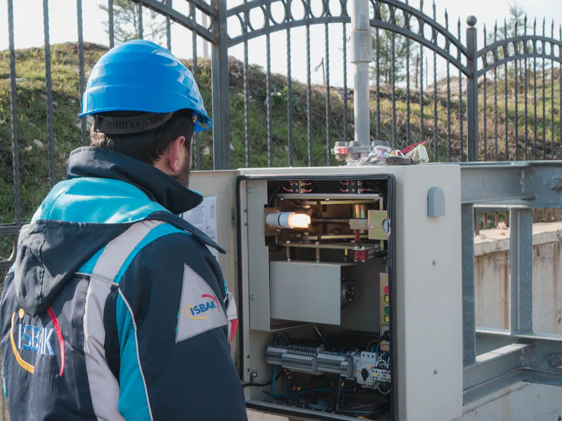 A professional electrician wearing a hard hat inspects an outdoor fuse box ensuring safety