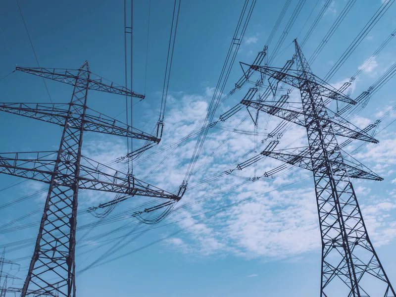 High voltage transmission towers stretch across a clear blue sky, symbolizing energy and industry
