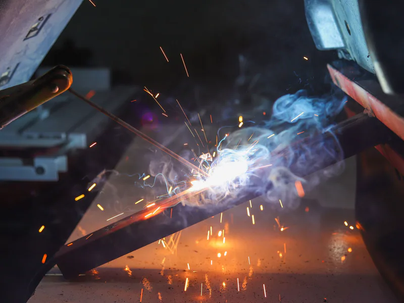 Close-up of a welder at work with sparks and smoke in an industrial setting