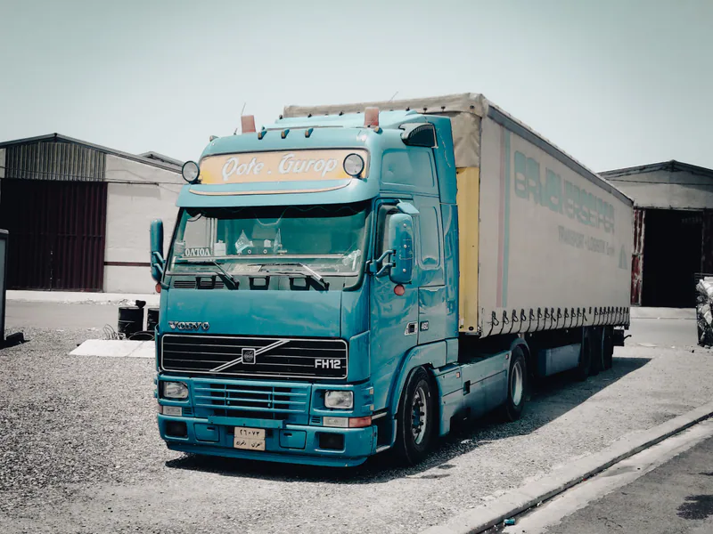 A blue Volvo truck parked outside a warehouse in an industrial area, daytime scene