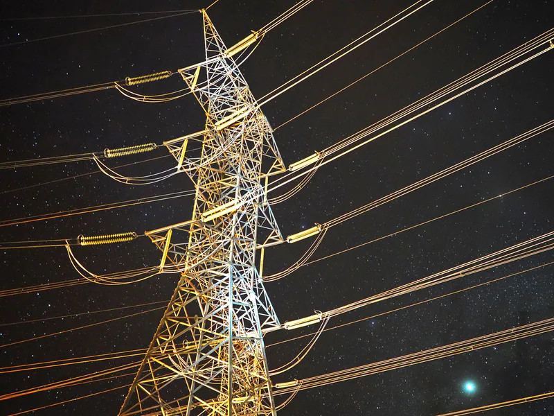 Illuminated power tower against a starry night sky, showcasing energy infrastructure
