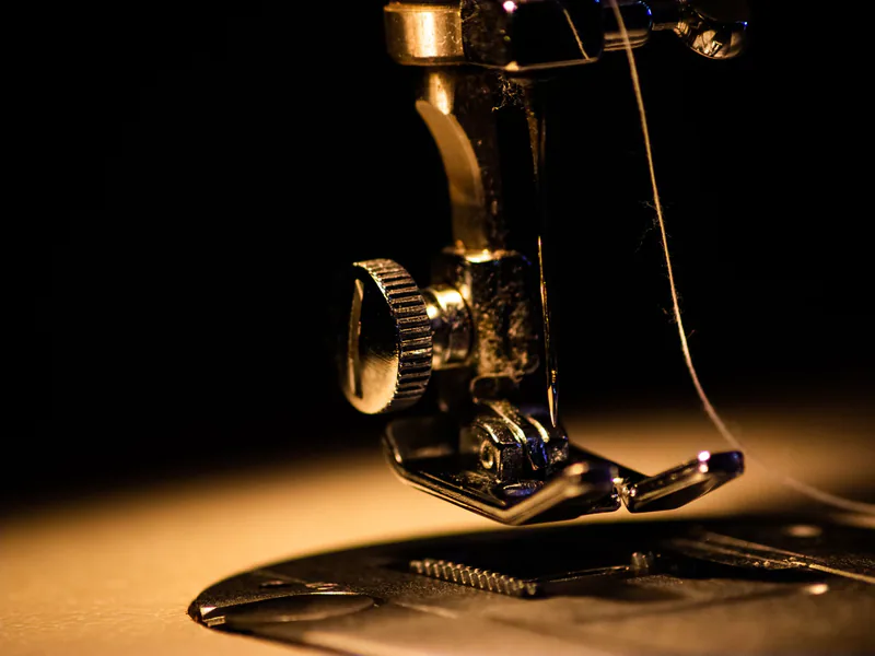 Detailed close-up image of a sewing machine with a threaded needle, perfect for textile and crafting themes