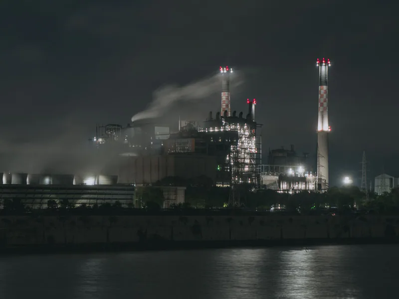 Night view of a large industrial factory with chimneys emitting smoke by the river in Ahmedabad, India