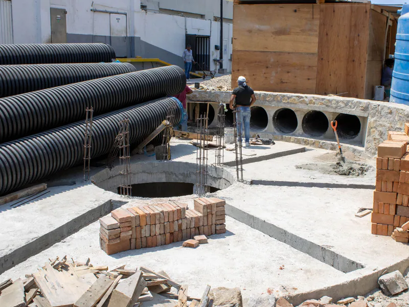 Workers at a construction site in Acapulco, Mexico, with stacked bricks and large pipes