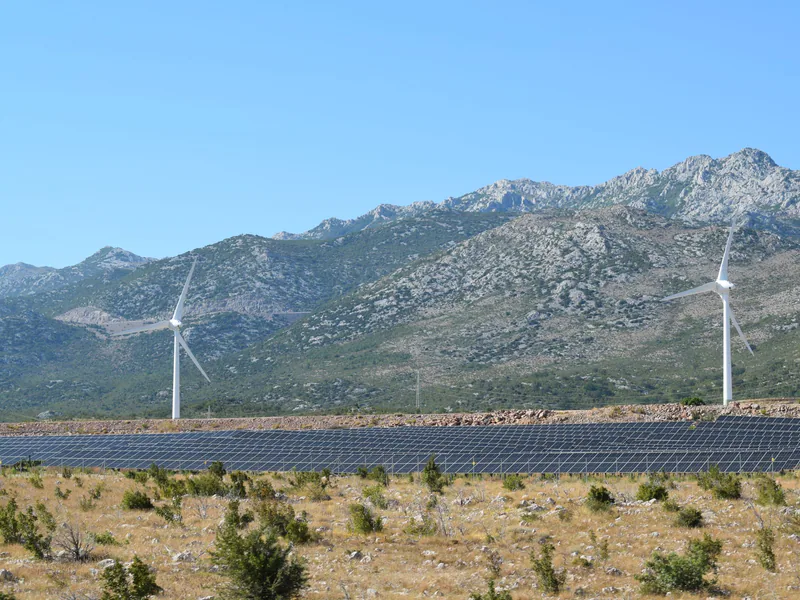A scenic view of windmills and solar panels against mountainous terrain under a clear blue sky
