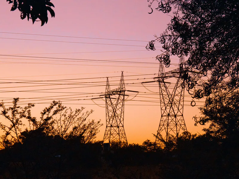 Silhouetted transmission towers at sunset surrounded by trees, creating an evocative scene