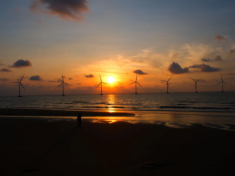 Silhouetted wind turbines against a vibrant ocean sunset create a serene coastal scene