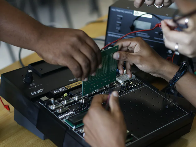Close-up of hands assembling an electronic circuit board, showcasing teamwork and technical expertise