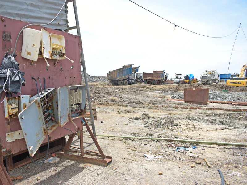 A barren construction site with rusted electrical panel and heavy equipment in the background