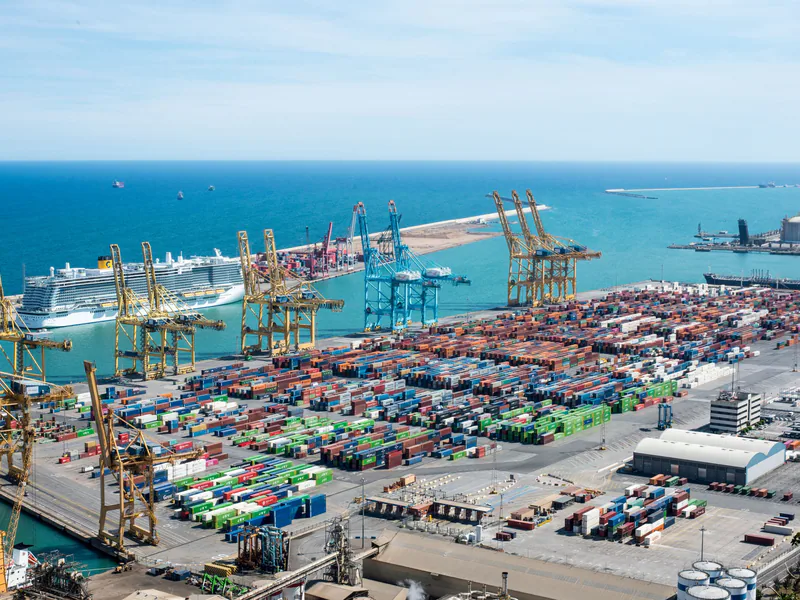 A vibrant aerial shot of Barcelona port featuring cranes, containers, and cruise ships on a sunny day