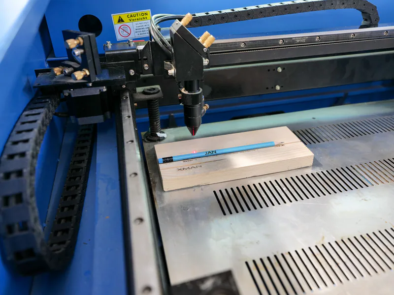 Laser engraving machine in action on wood with pencil for precise marking