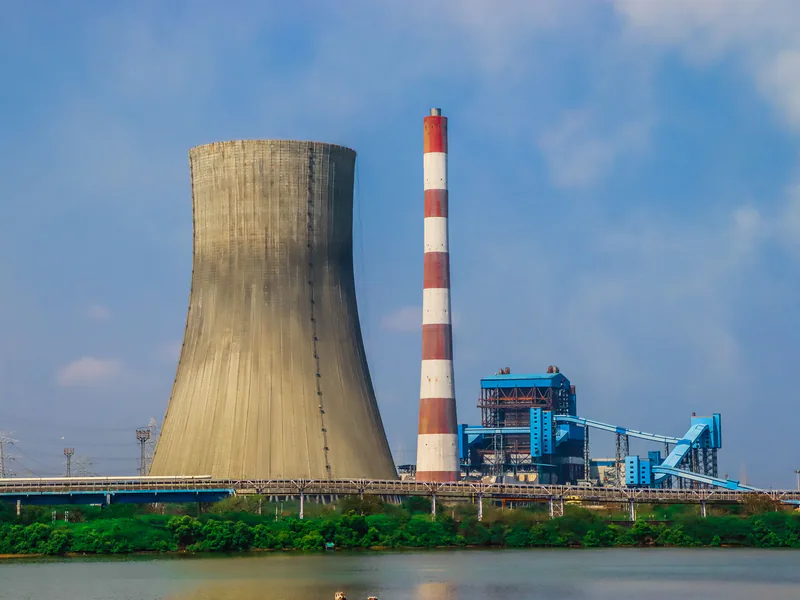 A large power plant with a cooling tower and a striped chimney by a river