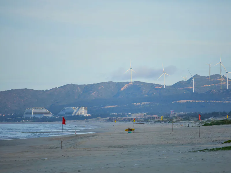 Tranquil beach view with wind turbines and distant mountains in Quy Nhon, Vietnam