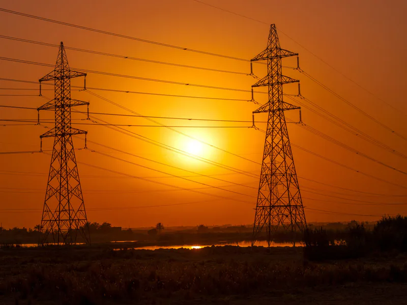 Silhouetted transmission towers under a vibrant sunset in Baghdad, Iraq