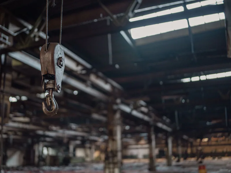 A detailed view of an industrial metal hook hanging inside a rustic warehouse